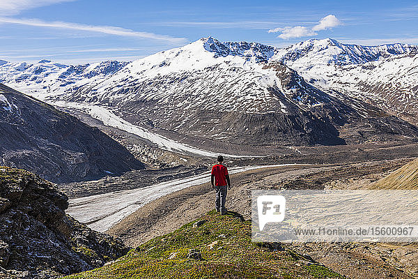 A man surveys Castner Glacier and the Alaska Range from the edge of an alpine meadow near Thayer Hut; Alaska  United States of America