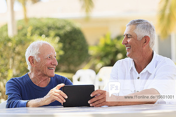 Ein älterer Mann zeigt seinem sehbehinderten Vater lächelnd ein digitales Tablet.