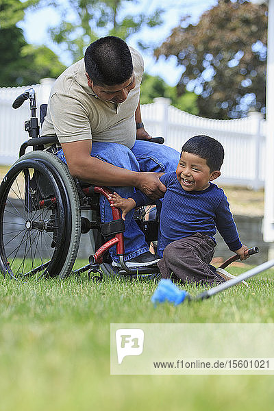 Hispanischer Mann mit Rückenmarksverletzung im Rollstuhl und sein Sohn bereiten sich auf das Waschen eines Autos vor