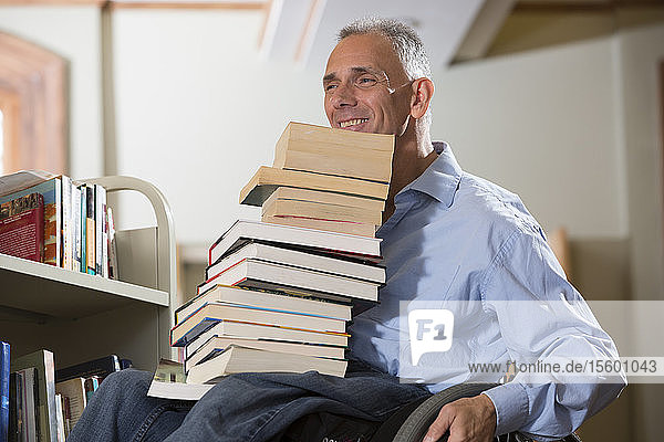 Mann mit Rückenmarksverletzung bewegt in einer Bibliothek zu viele Bücher