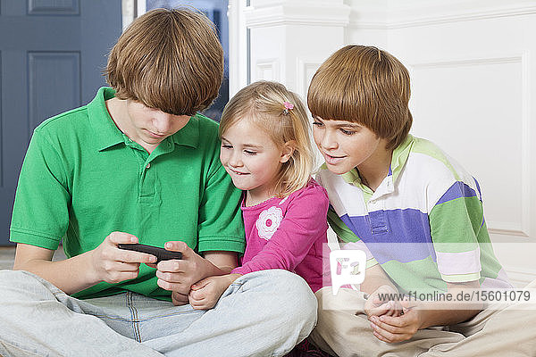 Mädchen und ihre beiden Brüder benutzen ein Smartphone