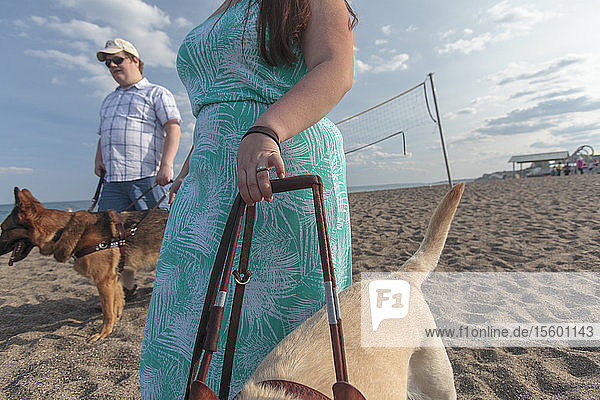 Young couple with visual impairments and service dogs walking along the beach