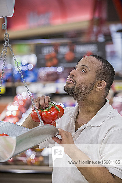 Mann mit Down-Syndrom beim Wiegen von Tomaten in einem Lebensmittelladen