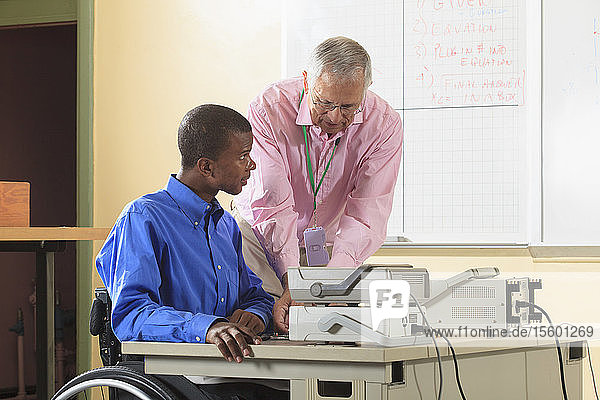 Ingenieurstudent im Rollstuhl sitzend bei der Vorbereitung eines Experiments im Elektroniklabor mit Professor