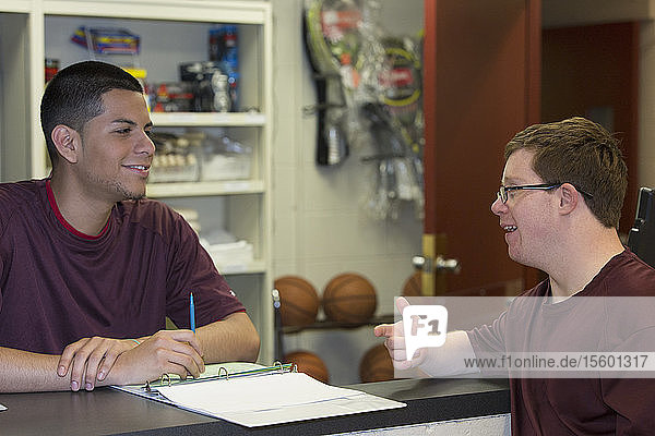 Young man with Down Syndrome working at college equipment dispensary for gym and talking to supervisor