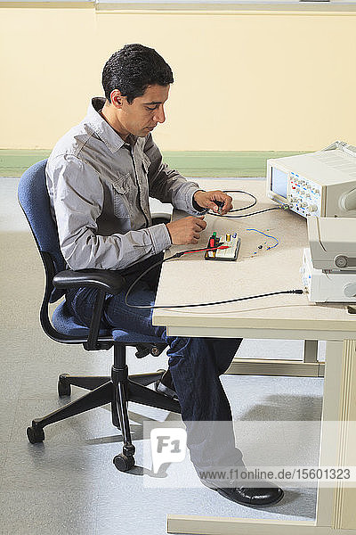 Ein Student der Ingenieurwissenschaften schließt ein Oszilloskop an ein Prototyping-Breadboard an  um ein Experiment für ein Elektroniklabor zu messen