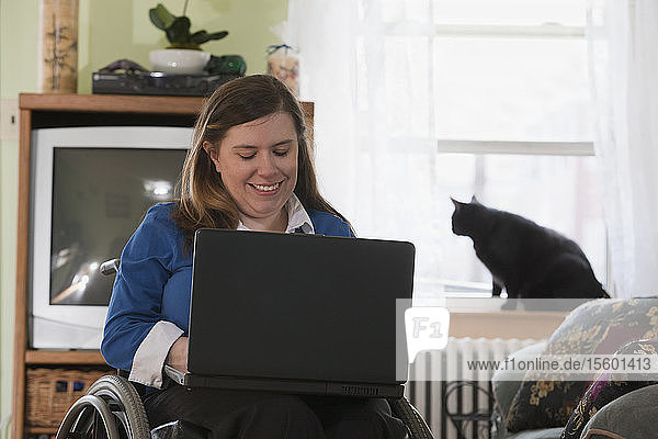 Geschäftsfrau mit Spina bifida im Rollstuhl benutzt zu Hause einen Laptop