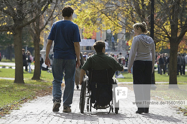 Rear view of a man sitting in a wheelchair with a man and a woman walking to a war protest