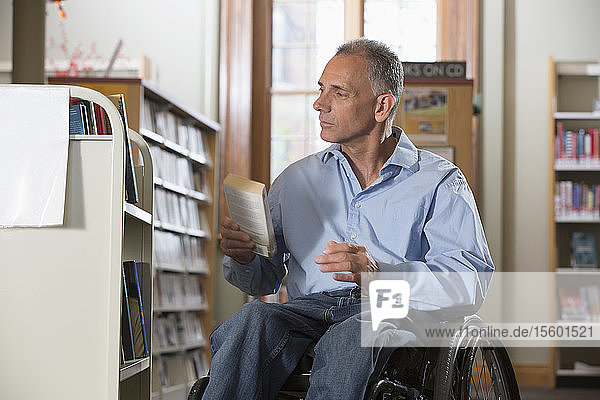Mann im Rollstuhl mit einer Rückenmarksverletzung ordnet Bücher in einer Bibliothek