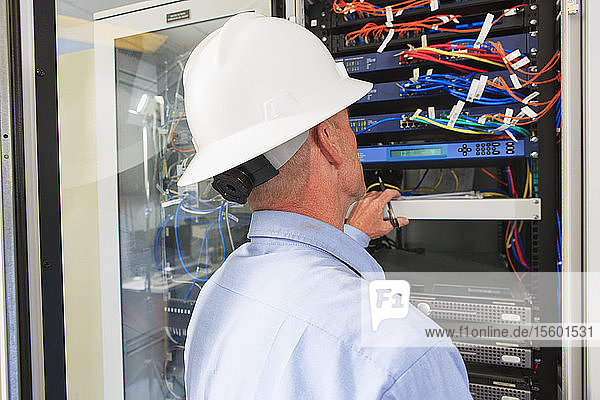 Engineer at electric power plant control room looking at servers and switches