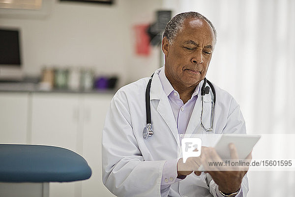 Nachdenklicher männlicher Arzt  der ein digitales Tablet benutzt  während er in seinem Büro sitzt.