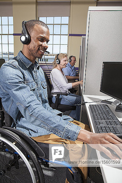 Mann mit Spinaler Meningitis im Rollstuhl bei der Arbeit an einem Stand in einem Callcenter