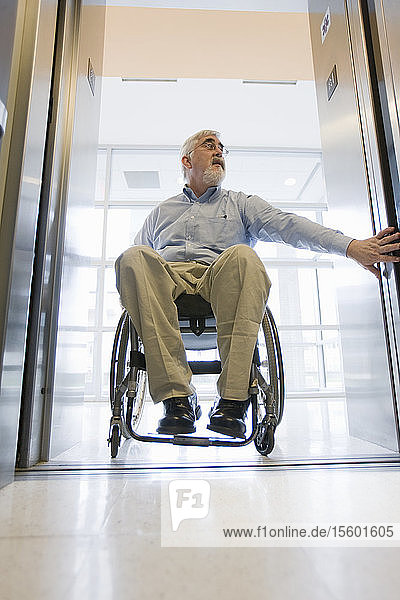 Universitätsprofessor mit Muskeldystrophie im Rollstuhl beim Betreten eines Aufzugs