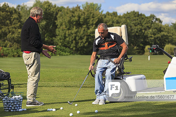 Golflehrer hilft einem Mann mit Rückenmarksverletzung beim Erlernen des Golfspiels