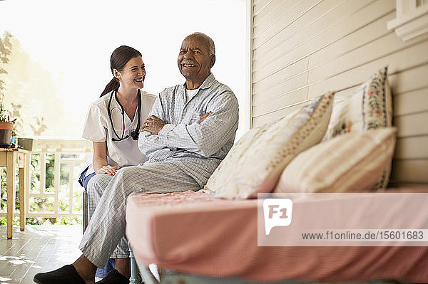 Lächelnder älterer Mann  der mit seiner Krankenschwester auf der Terrasse des Altenheims sitzt