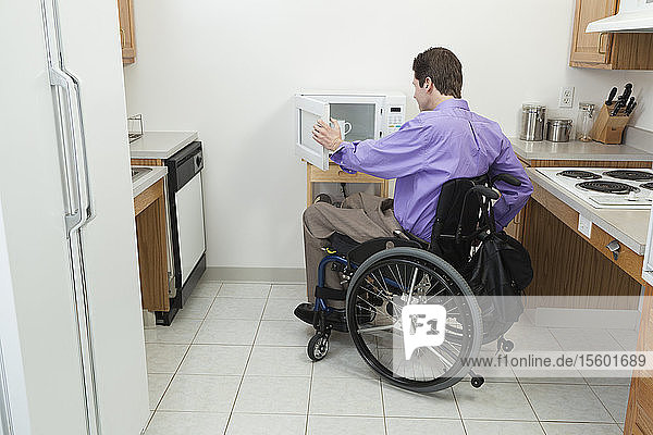 Mann im Rollstuhl mit Rückenmarksverletzung öffnet zugängliche Mikrowelle