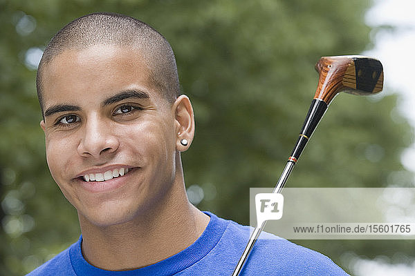 Porträt eines Teenagers  der einen Golfschläger hält und lächelt