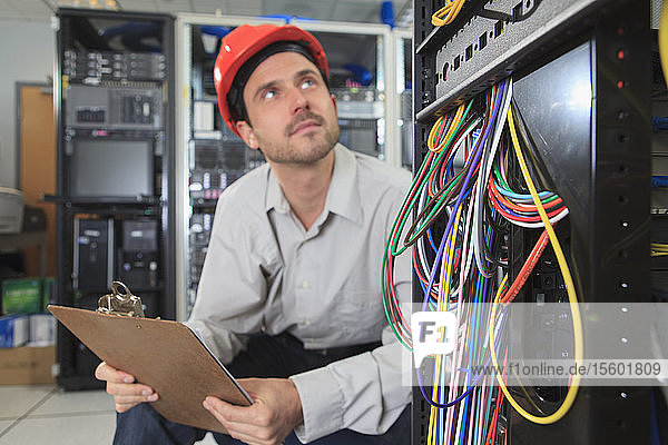 Network engineer with clip board reviewing control systems in data center
