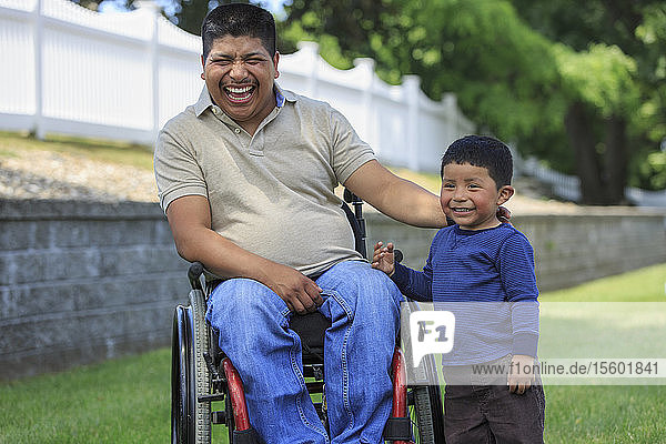 Hispanischer Mann mit Rückenmarksverletzung im Rollstuhl mit seinem Sohn lachend auf dem Rasen