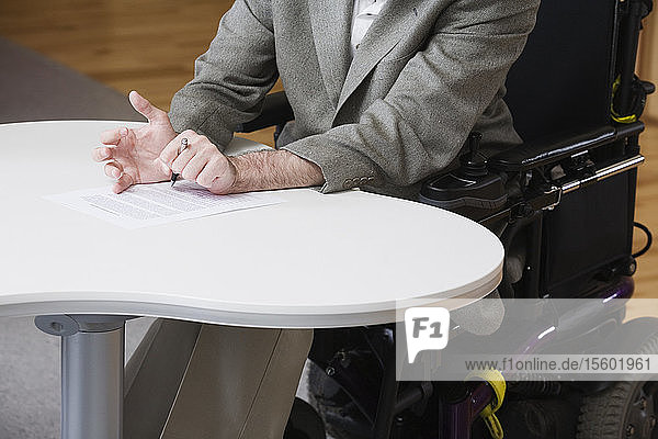 Älterer Mann mit zerebraler Lähmung beim Unterschreiben eines Dokuments