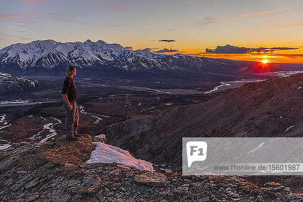 A hiker observes sunset from a mountain ridge in the Alaska Range; Alaska  United States of America