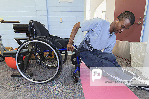 Ein Mann mit Rückenmarkshautentzündung steigt vom Yoga-Pad in seinen Rollstuhl