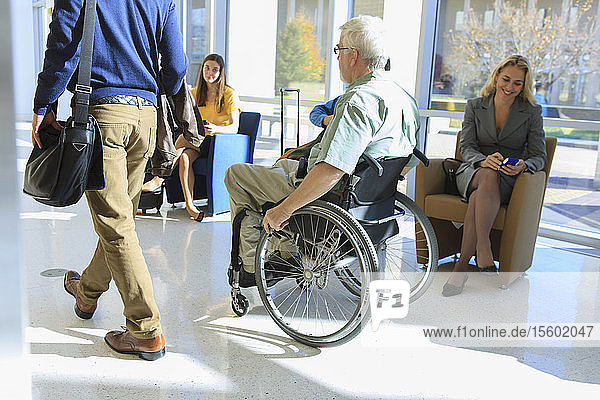 Mann mit Muskeldystrophie im Rollstuhl geht mit einem anderen Passagier in einem Flughafenkorridor spazieren