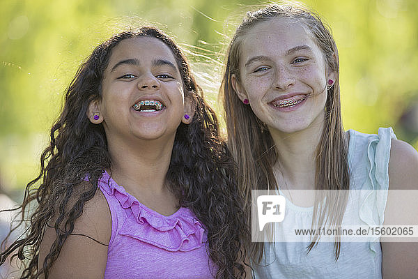 Portrait of two Hispanic teen sisters smiling with braces in a park