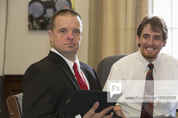 Man with Down Syndrome working as a Legislative Assistant holding a tablet with his colleague in the State Capitol office