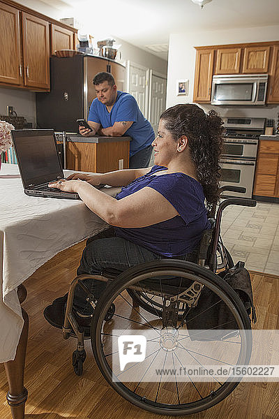 Frau mit Spina Bifida am Computer mit ihrem Mann beim Telefonieren zu Hause
