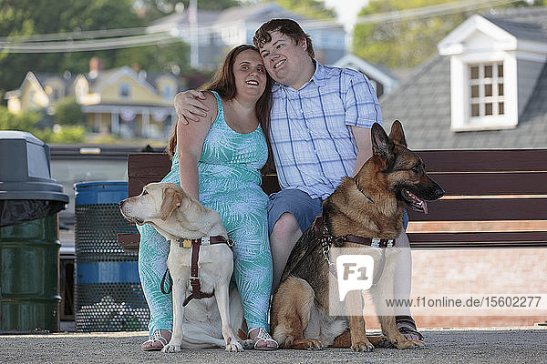 Ein blindes Paar  das sich mit seinen Diensthunden umarmt und auf einer Bank am Strand entspannt