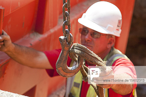 Construction worker placing lifting strap on hook