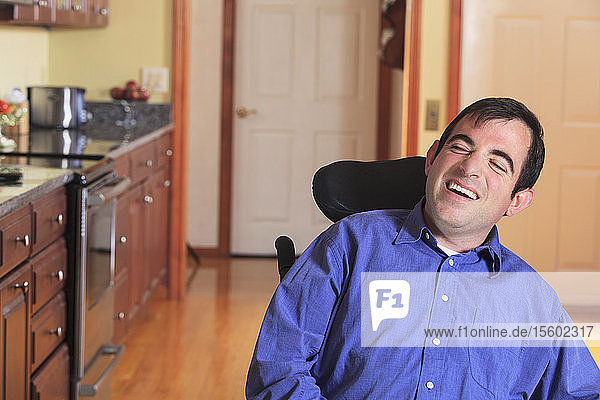 Mann mit zerebraler Lähmung in seinem motorisierten Rollstuhl in seiner Küche