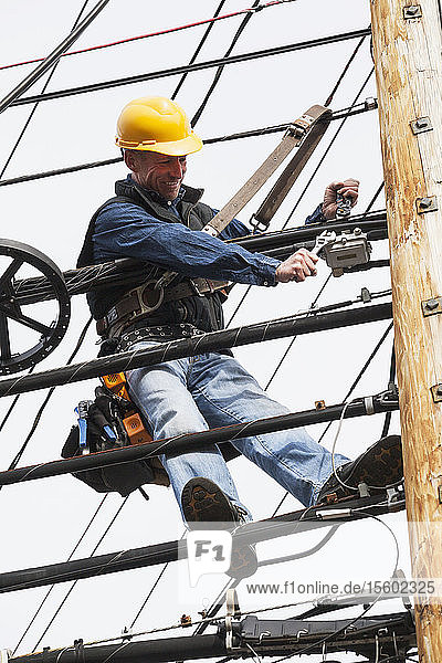 Arbeiter in der Kommunikationsbranche  der eine Combiner Box an hängenden Kabeln befestigt