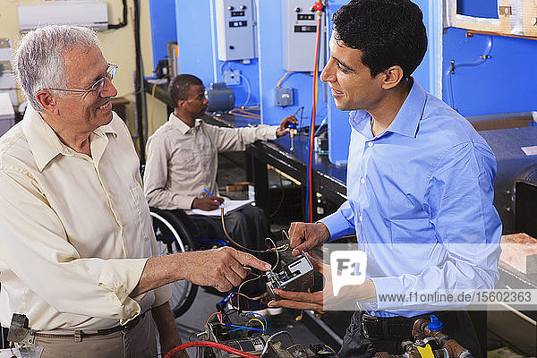 Student examining electrical control system on furnace with professor in HVAC classroom one student in wheelchair