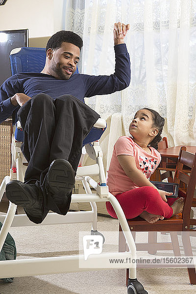 Afroamerikanischer Mann mit zerebraler Lähmung und seiner Tochter  die zu Hause ein Tablet benutzt