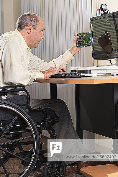 Mann mit Friedreich-Ataxie und deformierten Händen als Elektronik-Designer an seinem Arbeitsplatz mit einer Leiterplatte