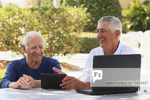 Ein älterer Mann zeigt seinem sehbehinderten Vater lächelnd ein digitales Tablet.