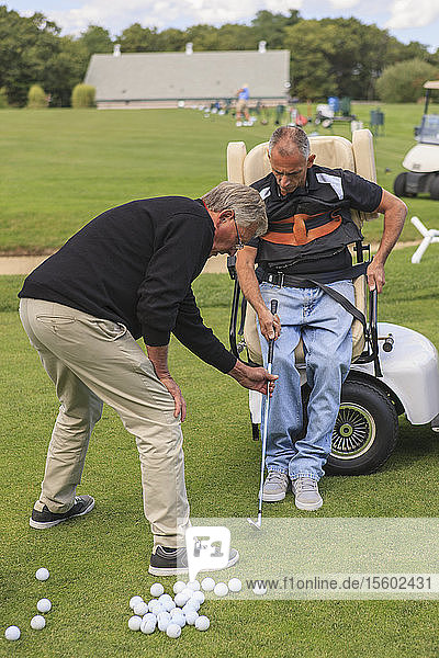 Mann mit Rückenmarksverletzung in einem adaptiven Wagen auf dem Golf-Putting-Green mit einem Ausbilder