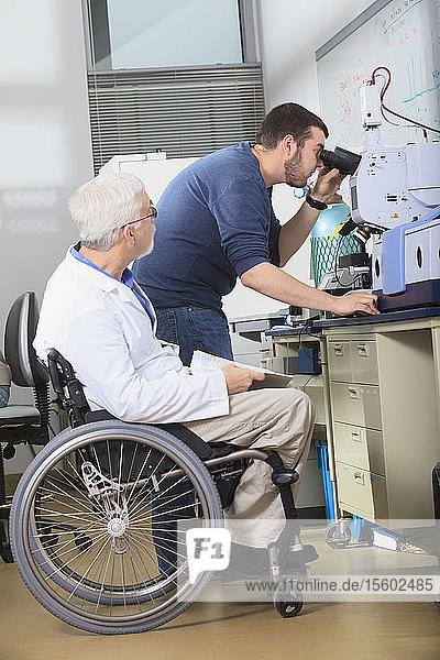 Professor mit Muskeldystrophie arbeitet mit einem Ingenieurstudenten zusammen  der in einem Labor einen Röntgenfluoreszenzanalysator untersucht