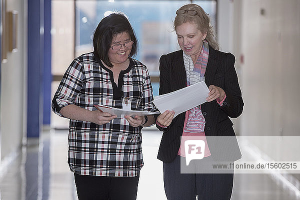 Asiatische Frau mit einer Lernbehinderung  die mit einem Kollegen Papierkram austauscht