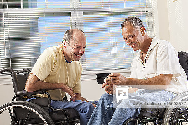 Zwei behinderte Männer sitzen in Rollstühlen und benutzen ein Smartphone