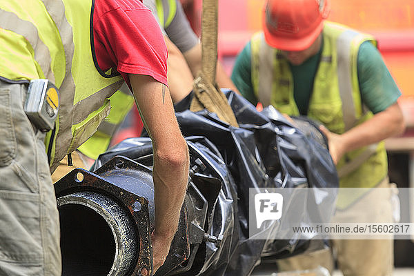 Construction workers guiding water main into place