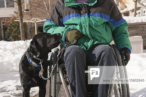 Frau mit Multipler Sklerose in einem Rollstuhl mit einem Diensthund im Schnee