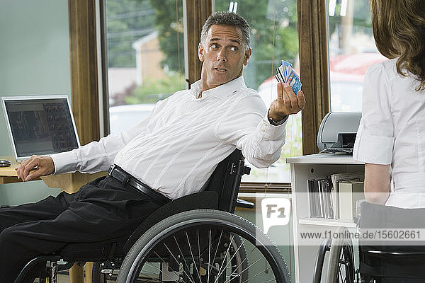 Ein älterer Mann und eine mittelalte Frau mit einer Rückenmarksverletzung sitzen in Rollstühlen und halten Kreditkarten in der Hand.