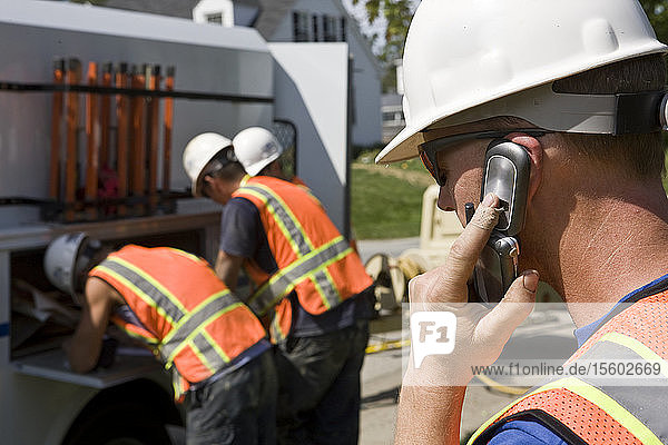 Bauarbeiter  der mit einem Mobiltelefon spricht  zwei Männer am Lastwagen im Hintergrund
