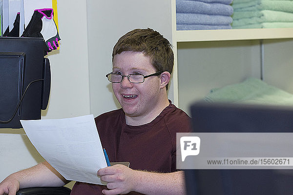 Young man with Down Syndrome doing paperwork at college equipment dispensary for gym