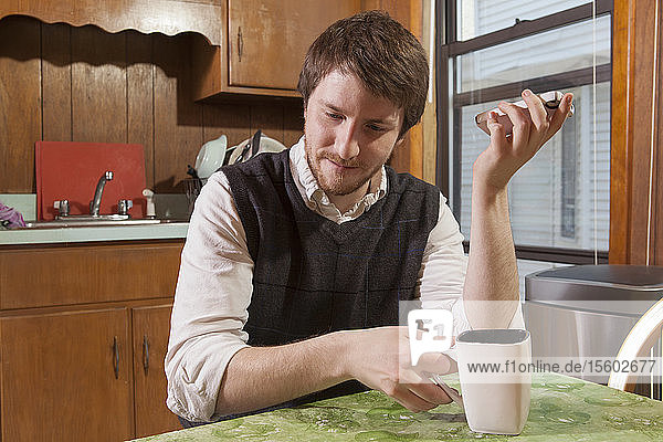 Blinder Mann in seiner Küche  der beim Kaffeetrinken Hilfsmittel auf seinem Mobiltelefon hört