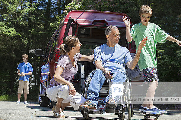 Mann mit Rückenmarksverletzung im Rollstuhl gibt seinem Sohn auf dem Skateboard ein High-Five