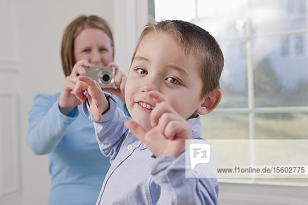 Junge  der das Wort Picture in amerikanischer Gebärdensprache gebärdet  während seine Mutter ein Foto von ihm mit einer Digitalkamera macht